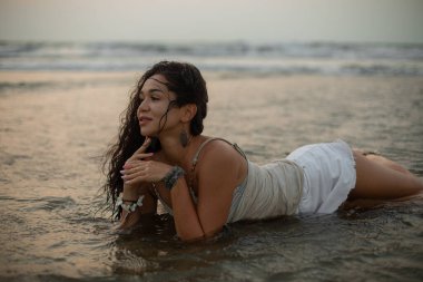 Güneşin batışına karşı deniz suyunda uzun ıslak saçlı, güzel, bronz tenli bir kadın. Doğadaki birlik. Deniz suyunun tadını çıkarıyorum. Turizm ve eğlence.. 