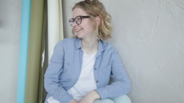 Młoda Kobieta Okularach Niebieskiej Koszuli Siedzi Pod Białą Ścianą Bawi — Wideo stockowe