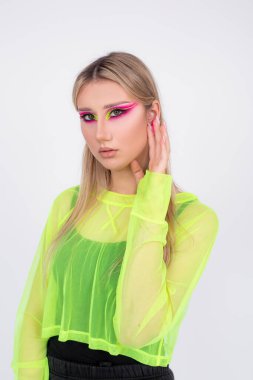 Diskolar ve partiler için yaratıcı gençlik imajı. Sarışın manken, parlak neon pembe ve açık yeşil tonlarda giyinir. Güzellik ve gençlik. Yüz sanatı. Modern moda trendleri. Portre. 