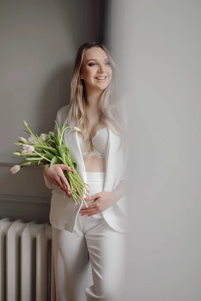 白いスーツの妊婦の笑顔は壁の近くに立つ新鮮なチューリップの花束を保持します 休日プレゼント 美しい春の花 ホーム女性の写真 選択的フォーカス 幸せな妊娠 若いお母さん — ストック写真