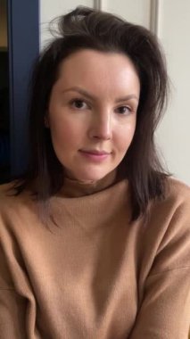 Mutlu kadın gün ışığıyla pencerenin yanında selfie çekiyor. Dikey ev kadını videosu. Pozitif ruh halinde, duygularını ifade eden ve gülümseyen bir genç bayanın portresi. Doğal makyaj, güzel insanlar..