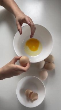 Dişi eller çiğ yumurtaları bir kaseye, yumurta kabuklarını diğerine koyar. Dikey pişirme videosu üst görünümü. Charlotte Pastası 'nın geleneksel tarifi, elmalı turta. Ev yapımı tatlı, Charlotte yemek yapıyor..