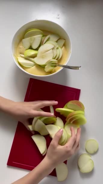 女性の手は生の生地でボウルに薄いリンゴスライスのヒープを置きます 垂直調理ビデオのトップビュー シャルロットケーキ アップルパイの伝統的なレシピ 自家製デザート シャーロット料理 — ストック動画