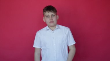 Virüs hastalığının ilk belirtileri. Stüdyoda kırmızı arka planda kısa kollu hapşıran beyaz gömlekli tatlı bir genç çocuk. Kameraya bakar. Yüz ifadeleri ve duygular. Virüs koruması. Tam HD görüntüler.