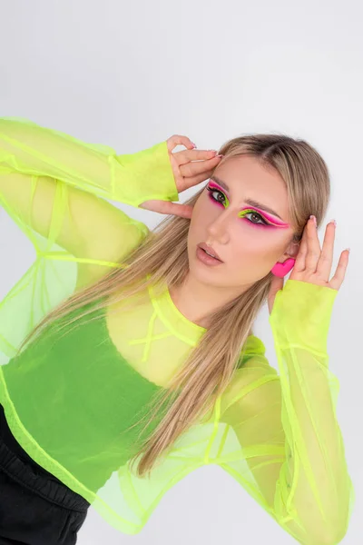 Shiny bright neon makeup. Face of woman is high fashion model in colorful bright neon pink and light green tones. Beautiful girl posing in studio on light background, colorful makeup.