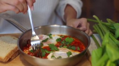 Beyaz kazaklı kadın, çatal kullanıyor, restoranda mükemmel pişirilmiş Shakshuka yiyor, yakınlarda bir buket çiçek var. Vejetaryen yemeği. Zevk alıyorum. Sağlıklı beslenme. - Öğle yemeği. Tam HD görüntüler