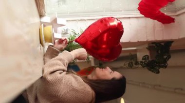 Genç ve güzel bir kadın, kafenin cam kenarında oturmuş elinde bir fincan kapuçino ve düşünceli bir şekilde kırmızı kalp şeklinde top oynatıyor. Sevgililer Günü. Mutlu anlar. Hediyeler ve eğlence. Tam HD görüntüler.
