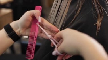 Uzun beyaz tırnaklı tanınmayan bir kadın kuaför kuaför kuaförü saç stili yapıyor, uzun ıslak, siyah saçlarını makasıyla kesiyor, kuaförde pembe plastik berber tarağıyla tarıyor..