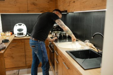 Kolunda dövme kollu, gözlüklü olgun bir adam fırın yapmayı öğreniyor, el yapımı turtalar, modern teknoloji mutfağında ekmek. Pişirme ve pişirme başlangıçları, ev kocası için yeni beceriler