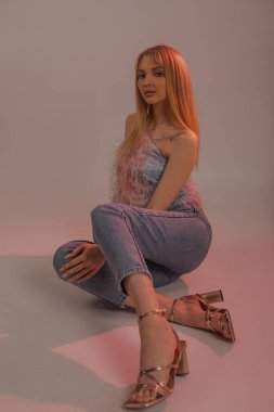 Dikey, baştan çıkarıcı, kendine güvenen, modern, çekici, günlük kıyafetleri olan sarışın kadın pembe karanlık stüdyoda kameraya poz veriyor. Alışveriş satışları, yeni botlar ve ayakkabı koleksiyonu. Lüks kıyafetler.