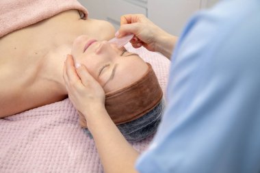 Kırpılmış kadın doktor elleri hasta yüzünü iyileştirir ve Çin güasası uygular, gua sha pembe yeşim taşı kazıyıcı aplikatörle yüz masajı kaldırır. Yüz şekillendirme ve şekillendirme. Yüksek açı görünümü