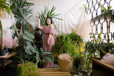 Kış bahçesi iç kısımda. Çekici genç bayan dairesinde yeşil cenneti gösteriyor. Hobi olarak. Çiçek işi. Bitki bakımı. Hayatın tadını çıkar. Olumlu duygular. Bitkilerin yetiştirilmesi ve bakımı. 