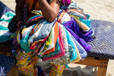 Kesilip tanınmayan koyu tenli bir kadın hareketli pazar sahnesinde bankta canlı renklerde türban satıyor. Kültür tarzını yükseltmek için modaya uygun ve uygun bir aksesuar..