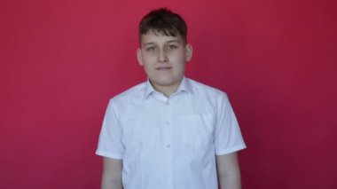 Kamera, neşe ve olumlu duygular gösteren 12 yaşındaki sevimli bir gence yakınlaşıyor. Stüdyo kırmızı arka plan. Kameraya bak. Neşe ve rahatlama. Yüz ifadeleri ve jestler. Tam HD görüntüler.