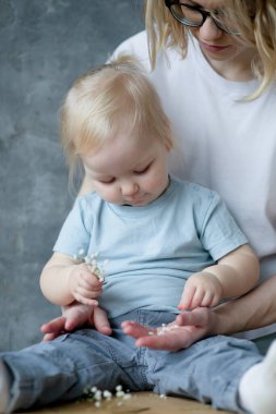 Gri mermer arka planda oynayan harika bir ailenin portresi. Genç, çekici bir kadın anne küçük, odaklanmış bir kız için küçük, beyaz, yapay çiçekler tutuyor. Kızları bukette toplanıyor. Annelik.