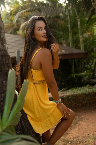 Vertical Mujer Morena Coqueta Sonriente Vestido Amarillo Apoyado Palmera Mirar — Foto de Stock