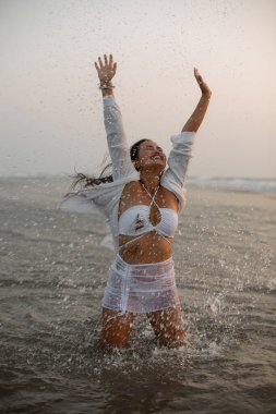 Gülümseyen Özgürlük ve sahildeki mutlu kadın fotoğrafı, okyanus yolculuğunun tadını çıkaran tatil, dingin insanlar, okyanus doğası, açık havada tatil. Asyalı güzellik. Gün batımı