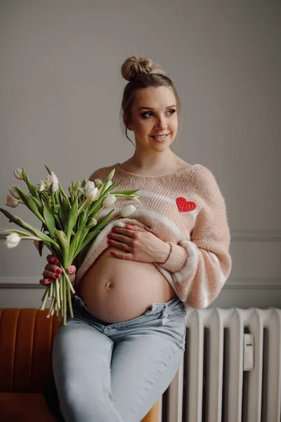 임신하고 엄마가 분홍색의 스웨터를 꽃다발을 임신부를 만지고는 미소짓는 바라본다 긍정적 — 스톡 사진