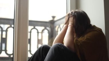 Orta yaşlı, çaresiz bir kadın pencerenin yanında oturuyor, uzun koyu saçlarını düzeltiyor, ellerini yüzüne kavuşturuyor, gözlerini kapatıyor, sorunlardan muzdarip. Depresyon, duygular, psikolojik sorunlar.