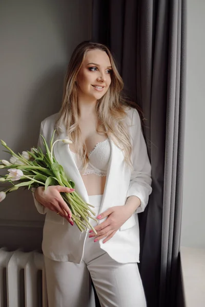 若い喜びの肖像画 妊娠中の女性は白いパンツ ブラジャーを着て 白いチューリップの花の花束を保持し ウィンドウを見て立っている — ストック写真