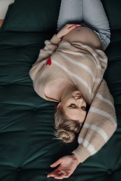 베이지 스웨터를 청바지를 에메랄드 침대에 채누워 즐거운 여자의 발가벗은 만지고 — 스톡 사진