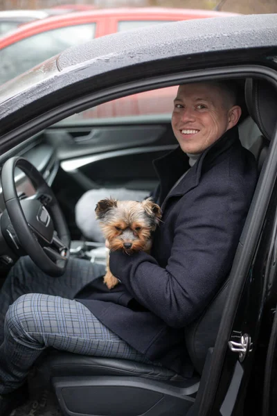 a portrait of handsome rich interesting funny intelligent man with dog where man is going to drive a car and sitting with opened door of his new car which was bought from his business money