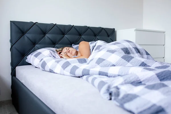 Attractive young woman is resting, sleeping in bed with padded headboard, in kapiton technique. Calm and serenity. Natural materials. Sound healthy sleep. Fatigue from work. Sleep is like medicine.