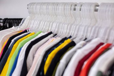 Erkekler spor için farklı boyutlarda pamuk t-shirtler giyer ve giyim mağazasındaki askılara asılır. Geniş bir kıyafet seçimi. Küçük bir iş. Yetişkin kıyafetleri. Parlak kıyafetler. Kıyafet indirimi..