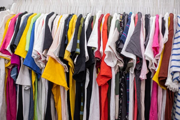 T-shirts of different colors and sizes for sports and summer hang on hangers in clothing store. Large selection of clothes. Small business. Adult clothing. Bright clothes. Clothing discounter.