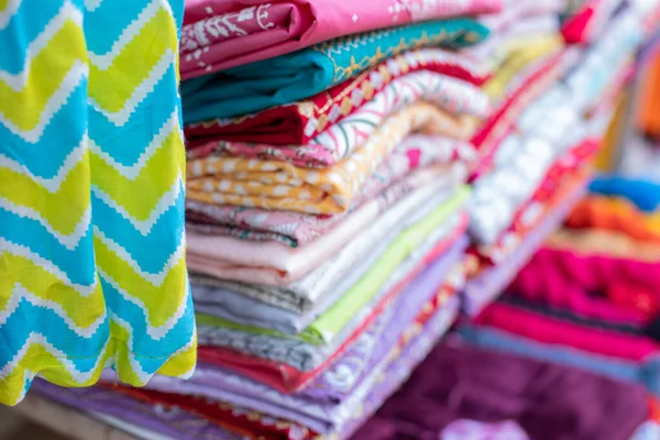 Fabric store, large selection. Bright multicolored fabrics with various patterns hang and lie in large piles on eastern market. Different textures of fabrics. Textile production and sale.