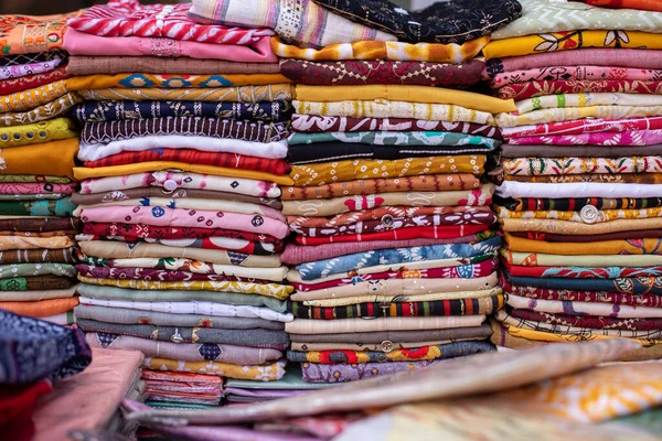 Huge selection of multicolored scarves, pareos, shawls, fabric cuts with various patterns lies of trading place, store, market. Natural raw materials. Cotton fabrics, satin, staple, viscose, cambric.