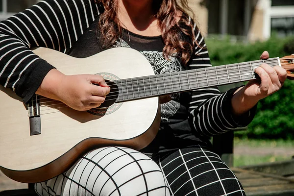难以辨认的人是一个穿着长袖套头毛衣的女人 她正在弹吉他 坐在城市广场的长椅上 孤独的人 精神健康 音乐疗法 课堂和业余爱好 音乐乐器 — 图库照片
