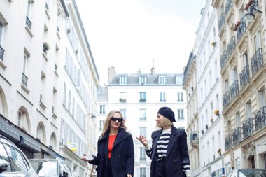 Paris 'te sokakta birlikte yürüyen iki kadın. Siyah elbiseli ve kırmızı dudaklı yetişkin sarışınlar tatilin tadını çıkarırken bir şeyleri tartışıyorlar. Kafasında bere olan kadın güneş gözlüklü kıza bak..