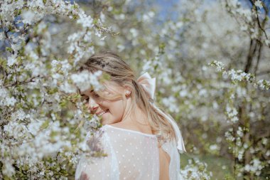 Gelinlik giymiş zarif bir bayan kiraz çiçekleriyle çevrili duruyor ve yumuşak bir gülümsemeyle geriye bakıyor. Koca saçlı genç gelin Sakura ağaçlarının yanında yürüyor ve güneşli günün tadını çıkarıyor..