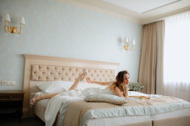 Otel odasında, beyaz gelinlik içinde, siyah saçlı görkemli gelin. Sıkıcı genç bayan, el pençe divan ayakta uzanmaya çalışıyor..