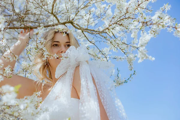 年轻女子穿着婚纱肩并肩站在白樱花旁 手持樱花枝条的画像 金发女士温柔地微笑着 望着远方 — 图库照片
