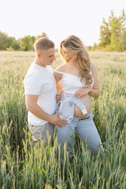 Genç bir bayanın hamileliği sırasında genç ve güzel bir çift yeşil çimlerin arasında yaz günü günbatımının keyfini çıkarıyorlar. Sevgi ve şefkat. Çocuk bekliyorum. Aile ilişkileri. Pozitif duygular. 