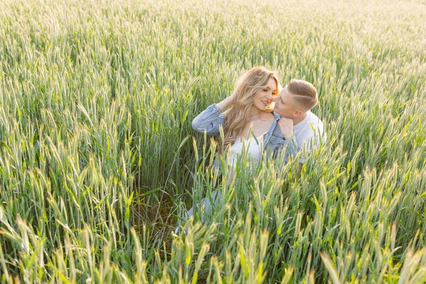 若い幸せな夫婦の背の高い緑の芝生の牧草地で晴れた日に座っている 抱擁し お互いを見ている 赤ちゃんを待ってる 素晴らしい瞬間だ 家族関係だ 肯定的な感情 — ストック写真