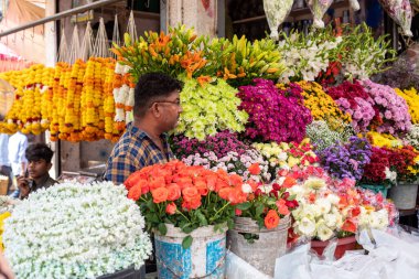 Goa, Hindistan, Şubat 2023. Orta yaşlı Hintli bir satıcının Hindistan 'da güneşli bir günde çeşitli renkli çiçeklerle tezgahta dikilmesinin yan görüntüsü..