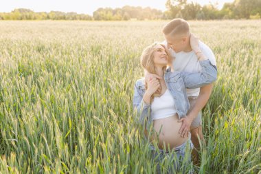 Çocuk bekliyorum. Genç bir kadının hamileliği sırasında genç evli bir çift çimenlerin arasında yaz gününün tadını çıkarıyor. Birbirlerine şefkatle sarılıp bakıyorlar. - Aile. Pozitif duygular.