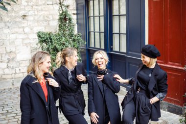 Bir grup gülen genç kızın portresi. Açık renk saçlı, siyah elbiseli, caddenin dışında duran, mavi renkli duvarların yanında duran, sohbet eden, alay eden, alay eden harika kadın arkadaşlar..