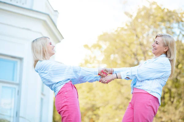 Positive emotions. Mom and daughter are spinning, hand in hand, on walk in park, they are dressed in identical pink trousers and blue shirts. Family relations. Closeness . Love and trust.