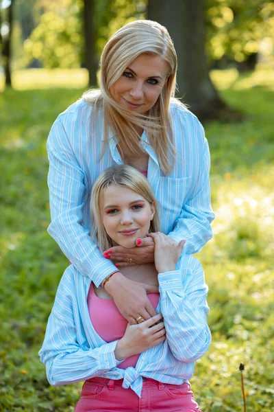 Beautiful portrait of mother and daughter on spring in park. They are dressed same, mom hugs her daughter. Family relations. Closeness and understanding. Love and trust. Connection of generations.