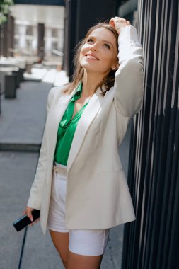 Güzel kahverengi saçlı kadın, serbest çalışan, iş kadını, yönetici elinde telefonla şehir caddesinde duruyor ve kafasını geriye doğru çeviriyor. Başarı ve kariyer. Modern iş kadınları. 