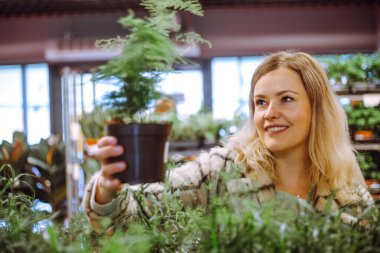 Uzun, lüks saçları olan sevimli sarışın bahçe merkezindeki hayran eğreltiotu örneklerine hayran. Kış bahçesi için gösterişsiz bitkiler. Hobi olarak. Harika bir hediye. Kış bahçesi ve sera. 