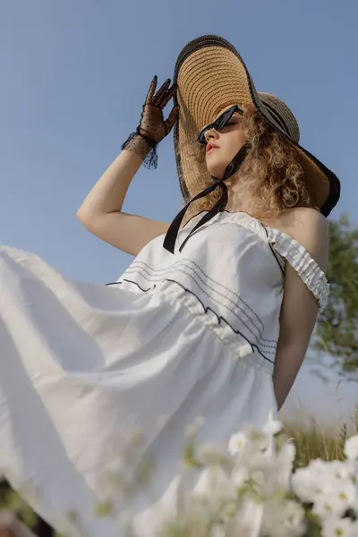 stock image Top view. Lovely young woman in snow-white summer dress, straw hat, black glasses against blue summer sky. Glamorous image. Skin care. Femininity and beauty. Conditioners and bleachers for laundry. 