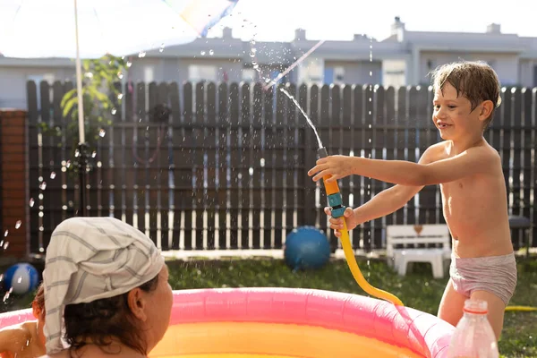快乐的男孩在阳光灿烂的夏天在充气游泳池附近玩水软管玩得很开心 有趣和娱乐 积极的情绪 快乐的童年夏天 — 图库照片