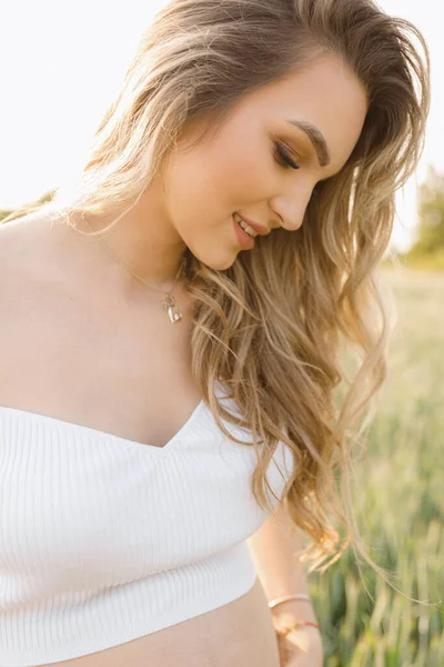 Close-up portrait of charming pregnant blonde with luxurious long loose hair on summer day in nature. Happiness and serenity. Healthy pregnancy. Positive emotions. Beauty and care.