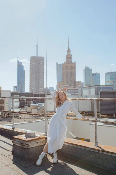 Recreation and tourism. Travel and impressions. Enjoying life and summer day is demonstrated by charming blonde in white dress with long luxurious hair, posing on roof of city building.