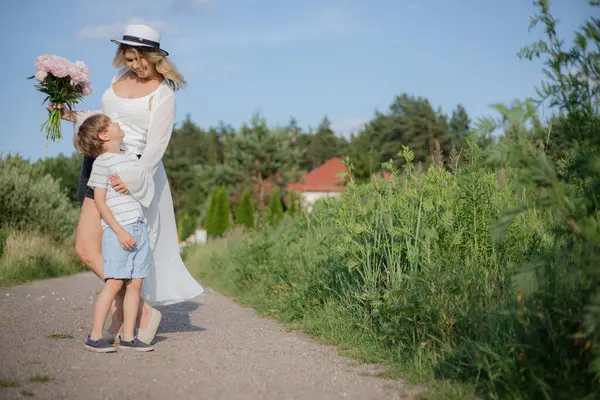 Happy mom and son enjoy each other on summer day in nature, walking along rural road. Positive emotions. Moms holiday. Single parents. Happy childhood. Family relations.